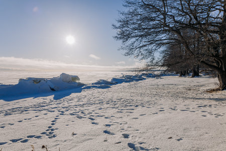 Winter landscape. Panoramic view of beautiful sunset on bay. Ice, snow and rocks on coastline. Setting sun in bright light. High quality photoの写真素材