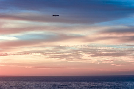 Plane in the sky is landing. Beautiful sunset in sky with clouds and rays of sunの写真素材