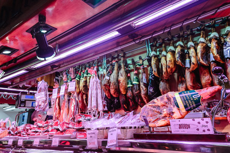 Barcelona, Spain - December 1, 2023: Barcelona market on La Rambla street. Spanish cured ham hanging...