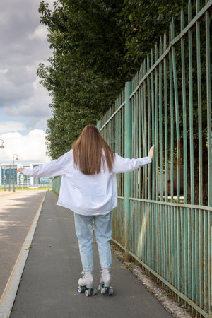 Beautiful girl with long hair rollerblading in park. Roller skating quads - popular and safe type of recreation. Vertical photo. High quality photoの写真素材