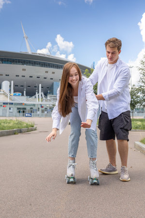 Young couple rollerblading and skateboarding in park. Happy and joyful girl and man doing sports together on warm summer day. Vertical photo. High quality photoの写真素材