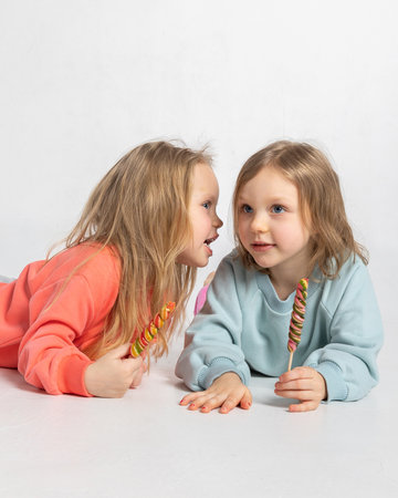Portrait of two beautiful cute little girls with sweets lollipop in their hands on light background. Vertical photo. High quality photoの写真素材