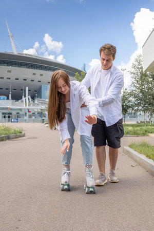 Young couple rollerblading and skateboarding in park. Happy and joyful girl and man doing sports...