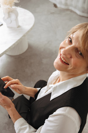 Portrait of business woman. Confident mature woman using mobile phone and typing on light gray background. Looking at camera. High quality photoの写真素材