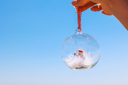 Woman's hand holds a Christmas ball on a beach sea background. Concept of New Year's holidays in exotic countries. Selective focus. High quality photoの写真素材