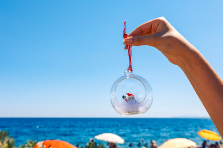Womans hand holds Christmas ball on beach sea background. Concept of New Years holidays in exotic countries. Selective focus. High quality photoの写真素材