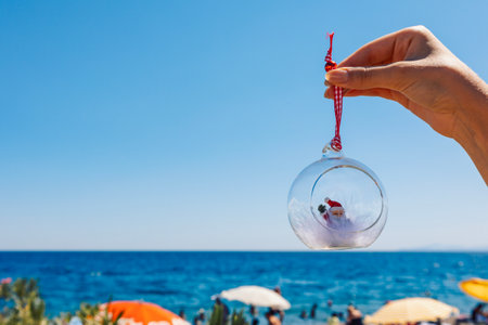Womans hand holds Christmas ball on beach sea background. Concept of New Years holidays in exotic countries. Selective focus. High quality photoの写真素材