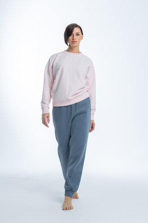 Beautiful woman of model appearance. Girl in light pink jumper and gray trousers on light background. Pretty female with trendy makeup posing in studio. Vertical photo. High quality photoの写真素材