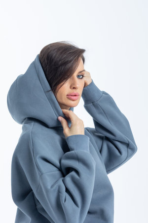 Portrait of a woman in a grey sweatshirt on a grey background. Female with trendy makeup posing in studio. Vertical photo. High quality photoの写真素材
