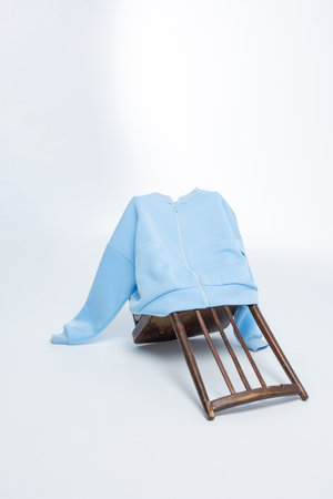 Light blue sweatshirt hanging on overturned wooden chair against light background. Vertical photo.の写真素材
