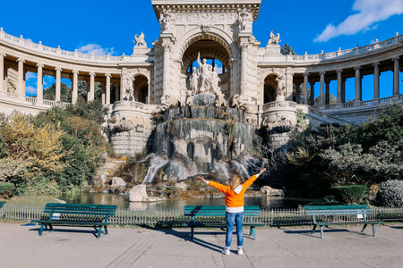 Woman in orange with her arms raised admires power of palace. View of beautiful Longchamp Palace complex with huge fountain, statues and flowering garden, Marseille, France. High quality photoの写真素材