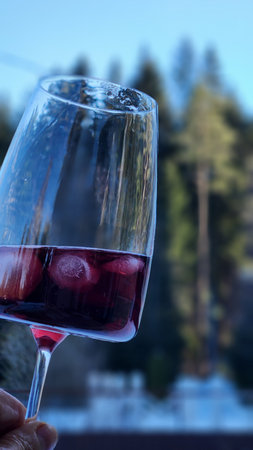 Female hand with glass of red wine against backdrop of nature. Vertical photo. High quality photoの写真素材