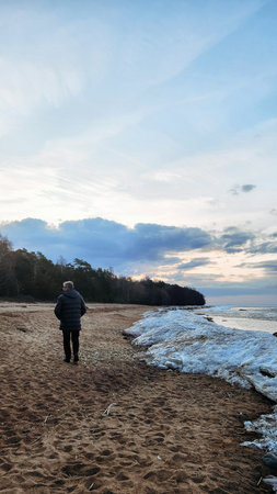 Panoramic view of beautiful dawn on bay. Cumulus clouds over water in bright light. Snow and rocks on coastline. Rising rays of sun are reflected in sea. Vertical photo.の写真素材