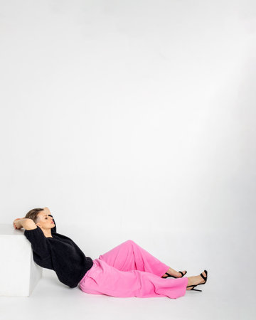 Portrait of a woman in black jumper and pink trousers on grey background. Female with trendy makeup posing in studio. Vertical photo.の写真素材