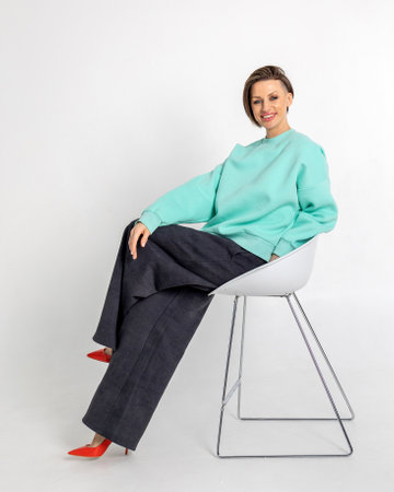 Portrait beautiful woman of model appearance. Girl in mint jumper, black trousers, red shoes on grey background. Pretty female with trendy makeup posing in studio. Vertical photo.の写真素材