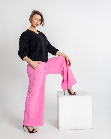 Portrait beautiful woman of model appearance. Girl in black jumper and pink trousers on grey background. Pretty female with trendy makeup posing in studio. Vertical photo.の写真素材