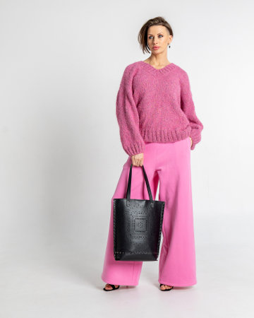 Portrait beautiful woman of model appearance. Girl in pink sweatshirt and trousers, black bag on grey background. Pretty female with trendy makeup posing in studio. Vertical photo.の写真素材