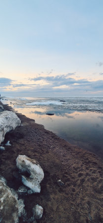 Peaceful scene of ice floes drifting in calm ocean waters with stunning sunset sky. Reflective water surface captures colorful clouds, evoking serenity and tranquility. Vertical photoの写真素材