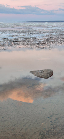 Peaceful scene of ice floes drifting in calm ocean waters with stunning sunset sky. Reflective water surface captures colorful clouds, evoking serenity and tranquility. Vertical photoの写真素材