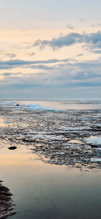 Peaceful scene of ice floes drifting in calm ocean waters with stunning sunset sky. Reflective water surface captures colorful clouds, evoking serenity and tranquility. Vertical photoの写真素材