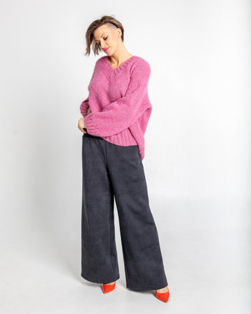 Portrait of a woman in a pink jumper, black trousers, and red shoes on a grey background. Pretty female with trendy makeup posing in a studio. Vertical photo.の写真素材