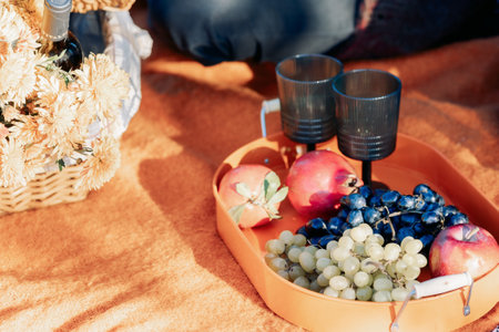 Autumn picnic on beach by sea. Fresh fruits, wine glasses, bottle, grapes, pomegranate near picnic basket on orange blanket. High quality photoの写真素材