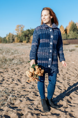 Female portrait. Beautiful young girl with long dark hair walking with bouquet of flowers along beach on sunny autumn day. Vertical photo. High quality photoの写真素材