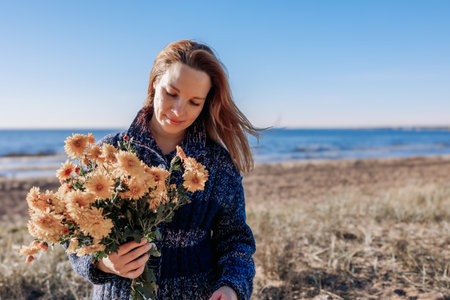 Female portrait. Beautiful young girl with long dark hair walking with bouquet of flowers along beach on sunny autumn day. High quality photoの写真素材