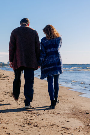 Loving couple walks on beach along sea on sunny autumn day. Weekend and lifestyle concept. Vertical photo. Back view. High quality photoの写真素材