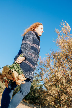 Female portrait. Beautiful young girl with long dark hair walking with bouquet of flowers along beach on sunny autumn day. Vertical photo. High quality photoの写真素材