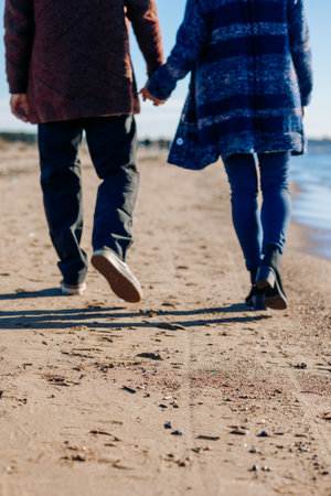 Loving couple walks on beach along sea on sunny autumn day. Weekend and lifestyle concept. Vertical photo. Back view. High quality photoの写真素材