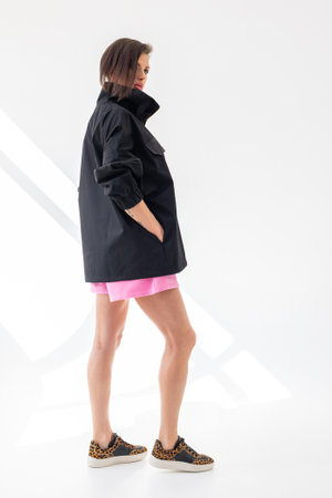Elegant woman in black windbreaker jacket and pink shorts on light background. Fashionable female style. Studio photography. Vertical photo. High quality photoの写真素材