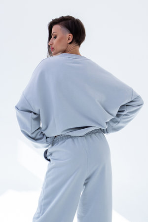 Young woman in gray sweatshirt and pants on white background. Studio photography. Vertical photo. High quality photoの写真素材