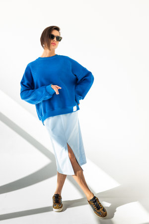 Elegant woman in blue sweatshirt and light blue skirt on white background. Fashionable female style. Studio photography. Vertical photo. High quality photoの写真素材
