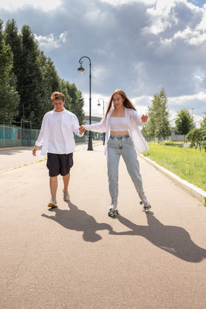 Young couple rollerblading and skateboarding in park. Happy and joyful girl and man doing sports...