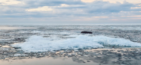 Peaceful scene of ice floes drifting in calm ocean waters with stunning sunset sky. Reflective water surface captures colorful clouds, evoking serenity and tranquilityの写真素材