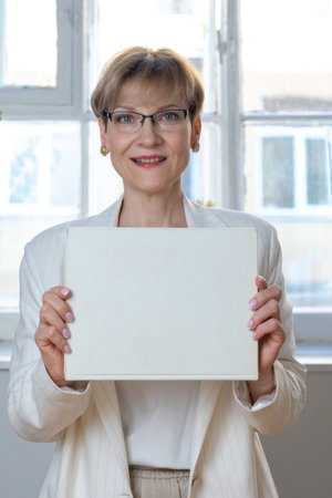 Portrait of emotional woman. Confident woman showing direction with hand on white sheet of paper with space for tex. Looking at camera, banner. Vertical photo. High quality photoの写真素材