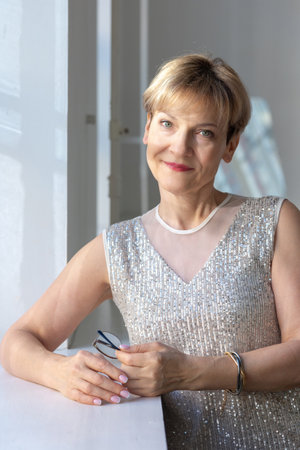 Portrait of smiling woman in festive clothes against a gray wall in a bright sunny room. Vertical...
