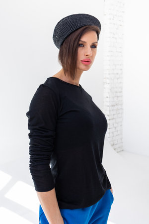 Elegant woman in black windbreaker jacket, blue pants and nautical hat on white background. Fashionable female in ocean French style. Studio photography. Vertical photo. High quality photoの写真素材