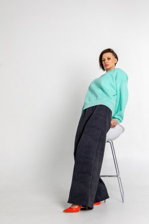 Portrait beautiful woman of model appearance. Girl in mint jumper, black trousers, red shoes on grey background. Pretty female with trendy makeup posing in studio. Vertical photo.の写真素材