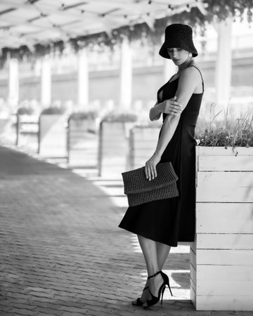 Beautiful elegant girl in hat stands at table in summer cafe, black and white photo. High quality photoの写真素材