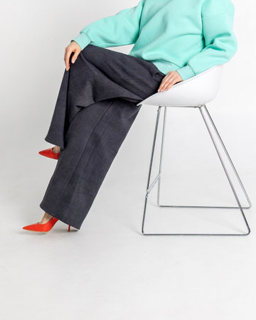 Beautiful woman of model appearance. Girl in mint jumper, black trousers, red shoes on grey...