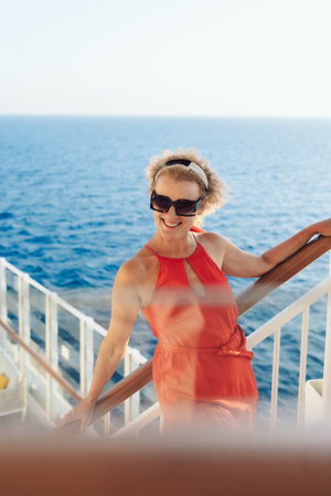 Beautiful happy woman on cruise ship deck. Elegant lady in red dress relaxing on vacation. Sea travel and summer holiday. Vertical photo. High quality photoの写真素材