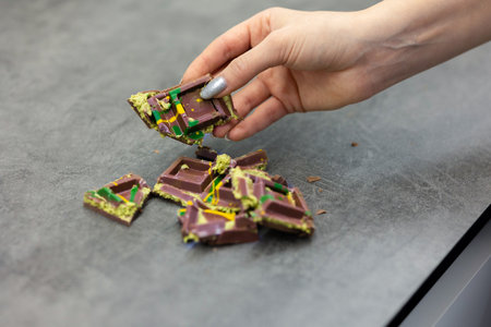 Womans hand holds piece of chocolate on gray background. Green kadayif and pistachio spread with pistachio in trend dessert. Close-up, selective focus. High quality photoの写真素材