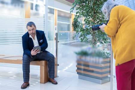 Female photographer shooting a businessman reading an ebook in a bright modern office. High quality photoの写真素材