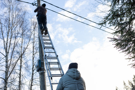 Male workers changing a burnt-out light bulb on light pole and operating at height on roadside utility structure in residential area outdoor scene.の写真素材