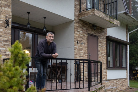 Adult male outdoors near home entrance, quiet pause, natural light, realistic lifestyle scene without emphasis on identity or location.の写真素材