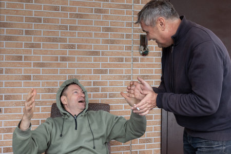 Two adult men arguing on outdoor wooden terrace near house expressing disagreement conflict and strong emotions.の写真素材