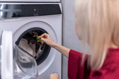 House hold. Female person using washing machine at home focusing on daily chores clean textiles and contemporary interior environment.の写真素材