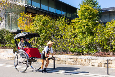 Kyoto, Japan - October 11, 2025: Rickshaw driver pulling carriage with tourists along sunny street...